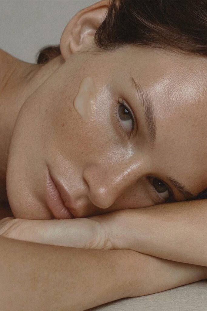 Model with radiant skin applying Daily Bloom serum on the cheek — visual representation of hydration, luminosity and the key benefits of the formula.